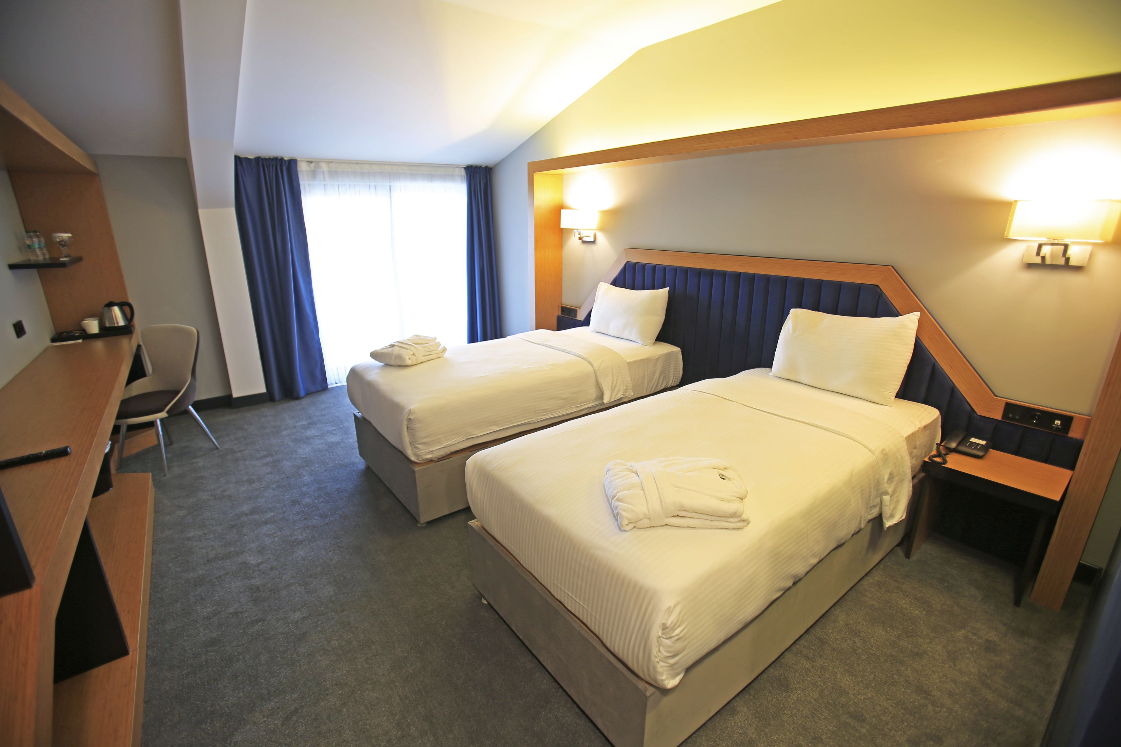 Een hotelkamer met twee bedden, een bureau, een stoel en een raam met gordijnen.