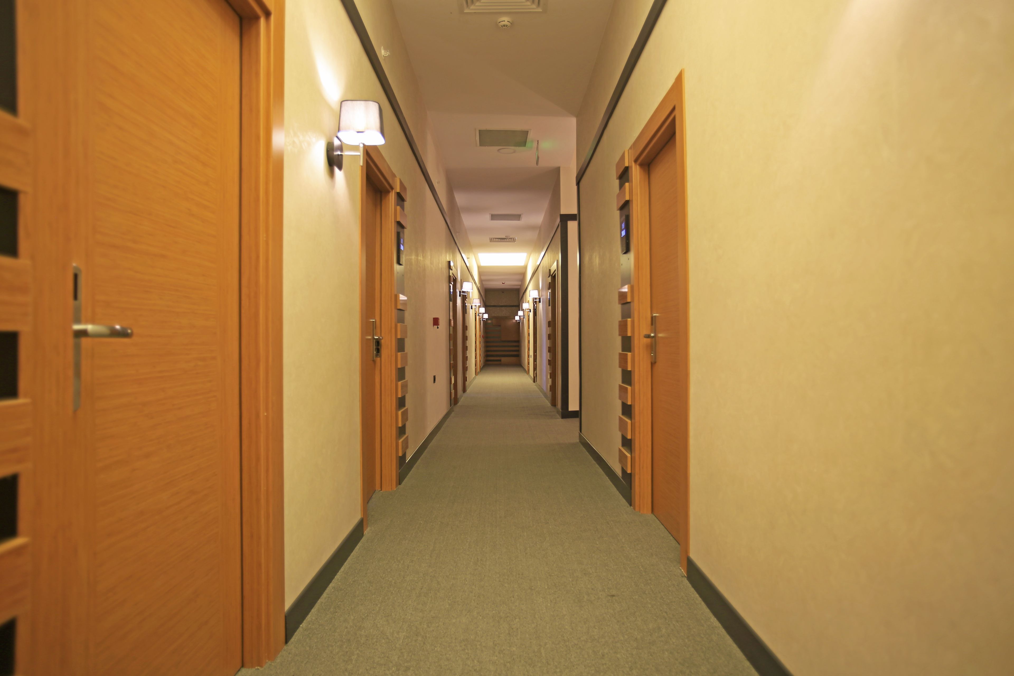 Un couloir d’hôtel avec des portes en bois, un sol recouvert de moquette et un éclairage au plafond.