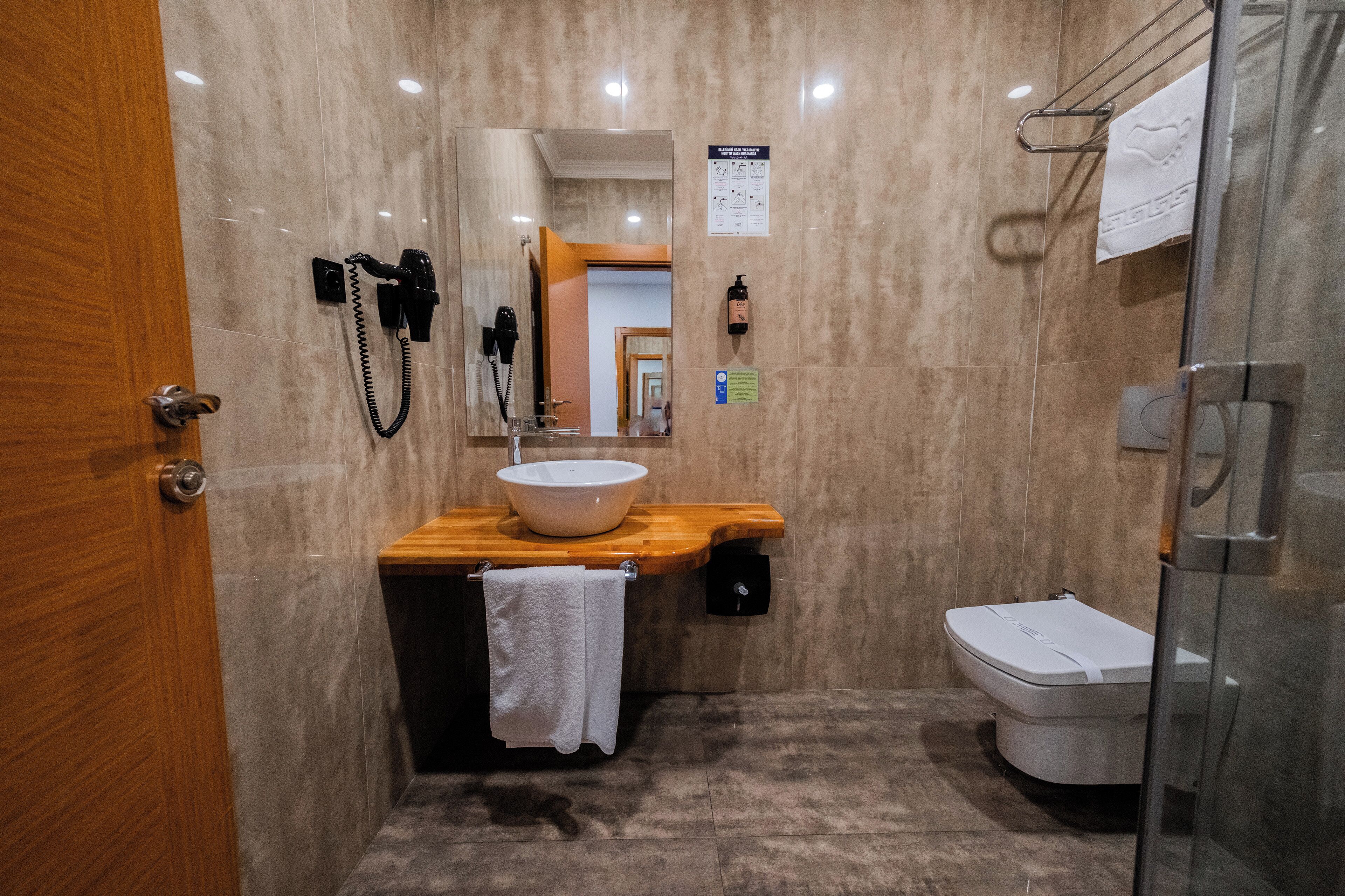 A modern bathroom with a wooden vanity, a white sink, a glass shower enclosure, and a toilet.