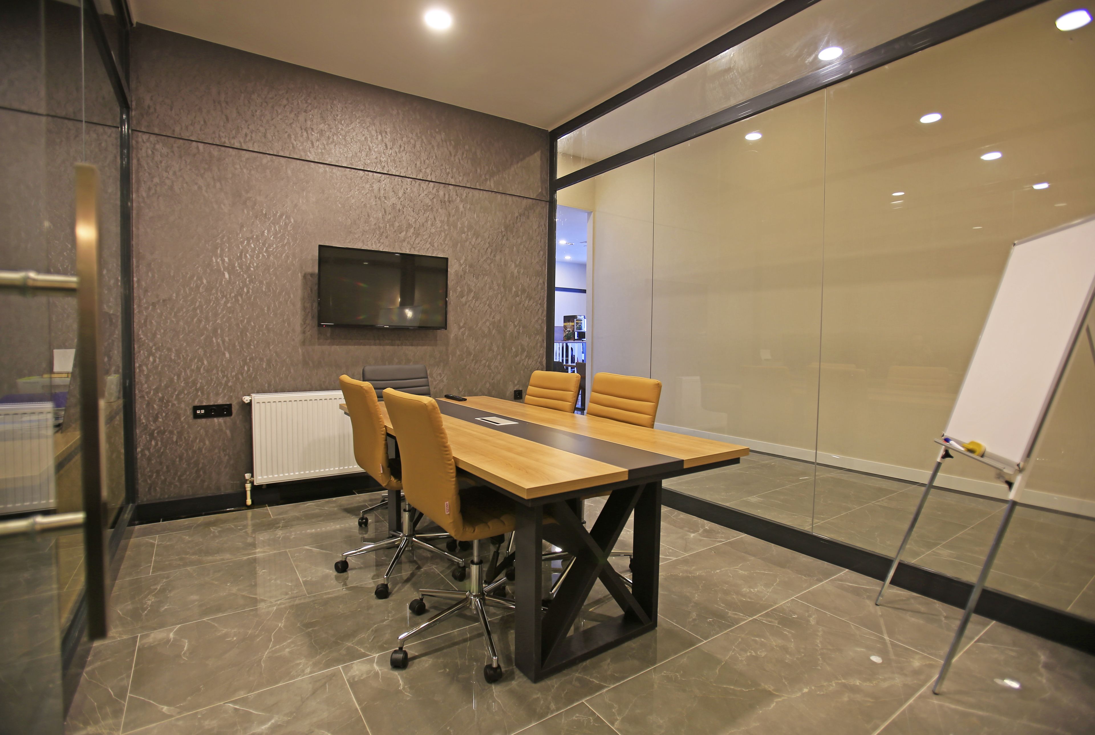 A conference room with a long table, chairs, a whiteboard, and a TV on the wall.