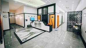 A modern hotel lobby with a reception desk, a digital screen, a patterned floor, and a decorative partition.