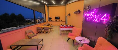 Un patio al aire libre con asientos, una mesa de fútbol de mesa y un letrero de neón.