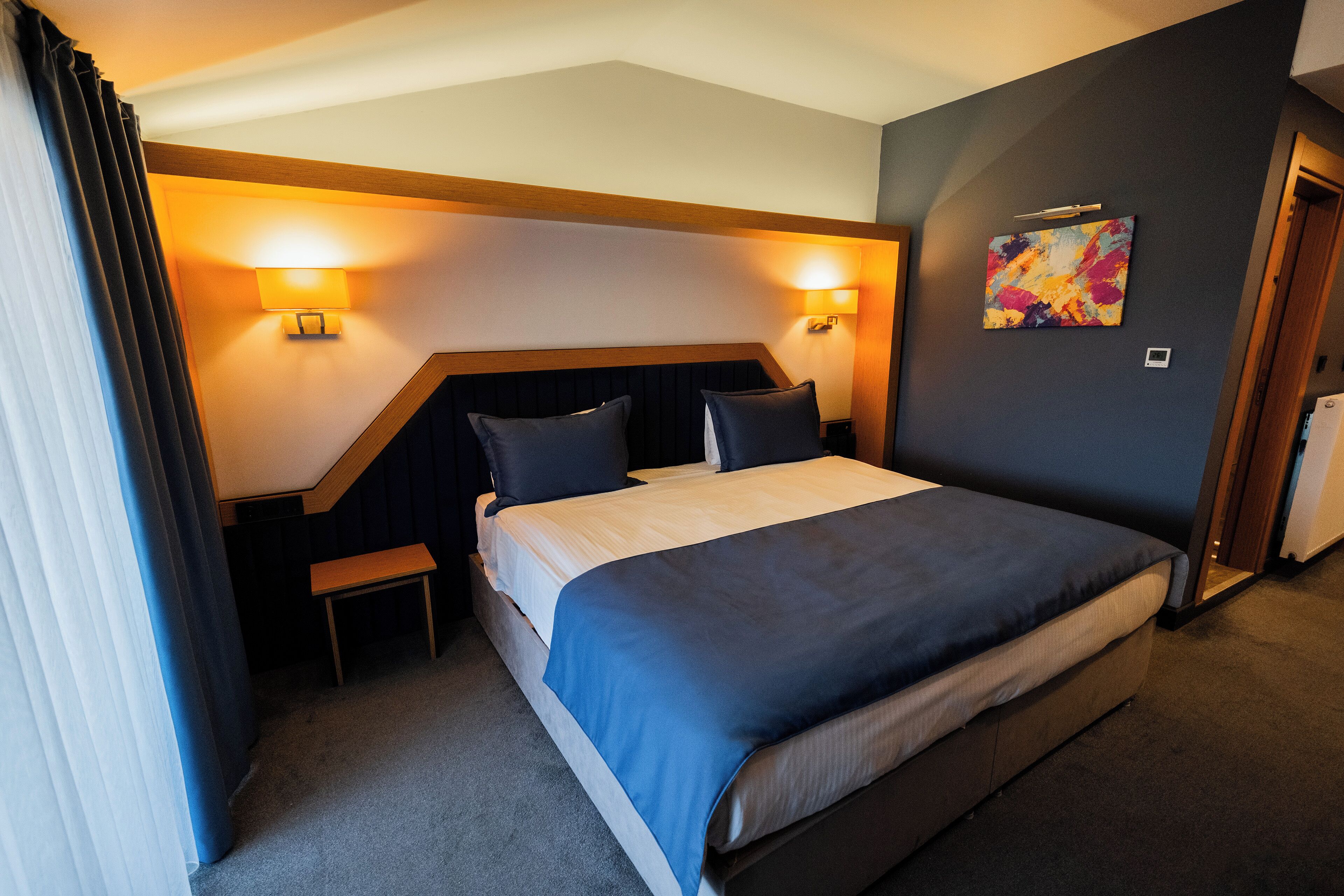 A hotel room with a bed, bedside tables, a bench, and a painting on the wall.