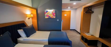A hotel room with two beds, a wardrobe, a television, and a painting on the wall.