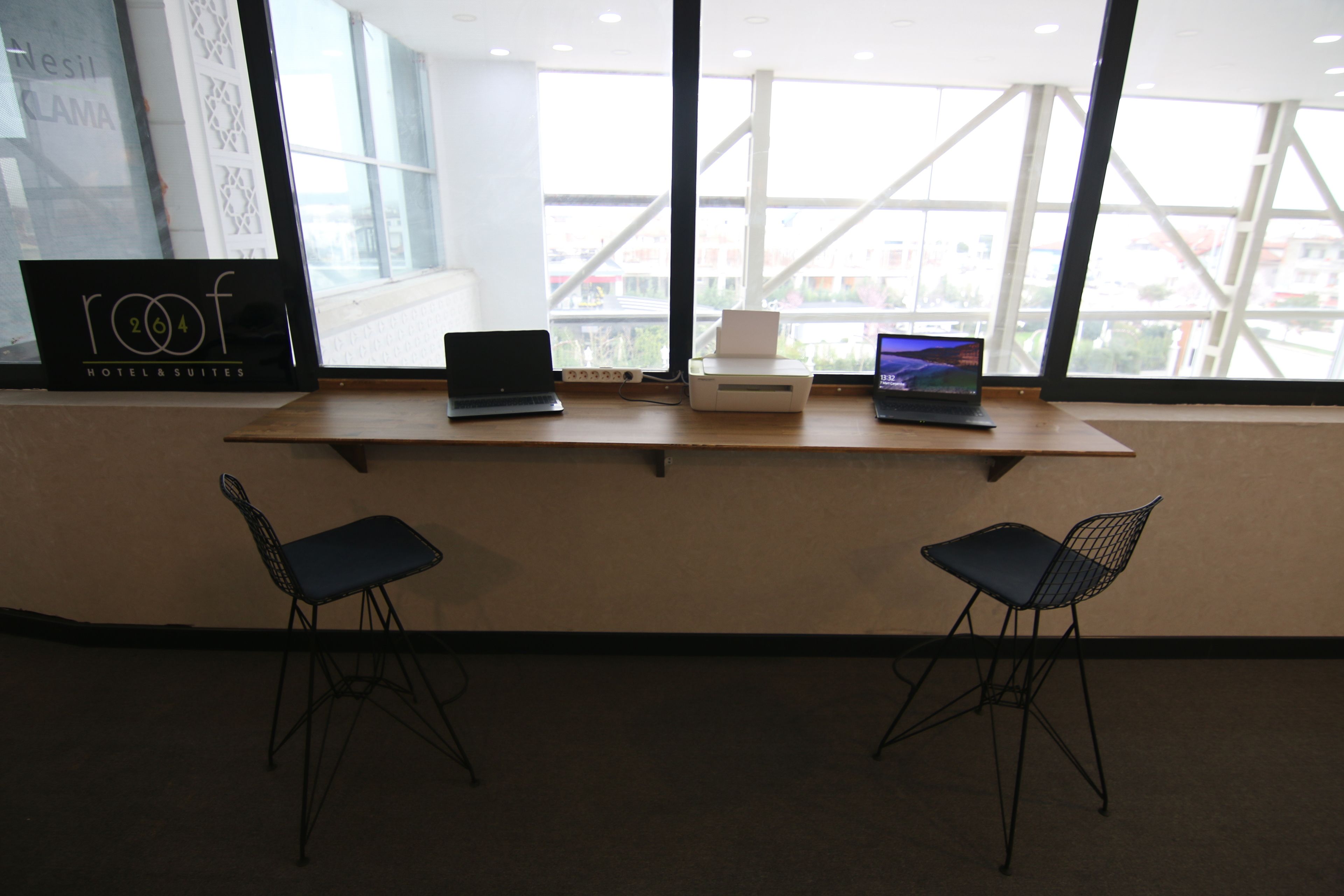 A modern hotel room with a large window, two black chairs, and three laptops on a wooden desk.