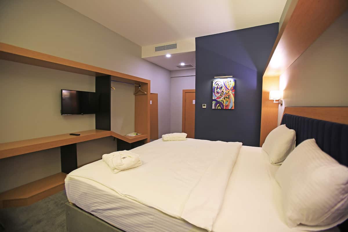 Une chambre d’hôtel équipée d’un lit, d’un téléviseur à écran plat, d’une œuvre d’art accrochée au mur et d’un banc en bois.