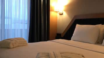 Habitación de hotel con una cama bien hecha, una lámpara de noche y una ventana con cortinas.