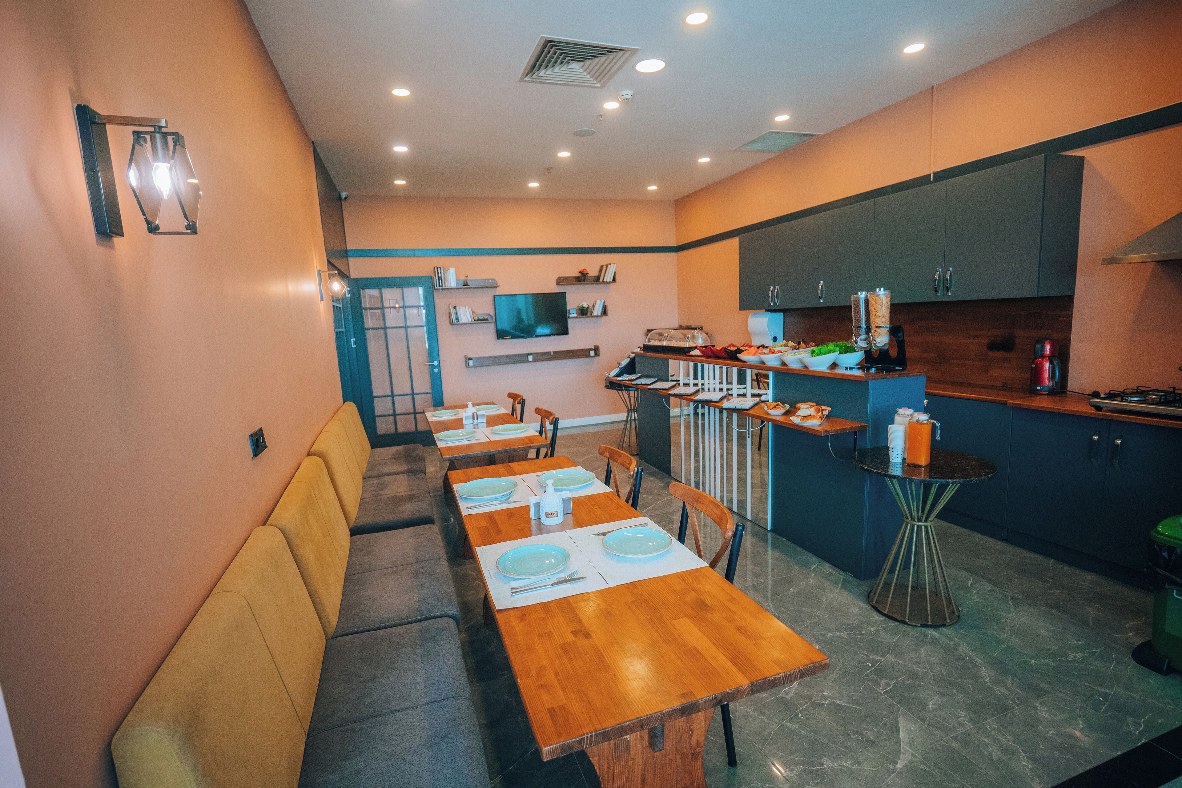 Una cocina moderna con armarios oscuros, una zona de comedor con mesas y sillas de madera, y una pequeña mesa redonda con una máquina de café.