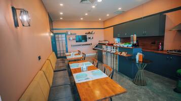 Una cocina moderna con armarios oscuros, una zona de comedor con mesas y sillas de madera, y una pequeña mesa redonda con una máquina de café.