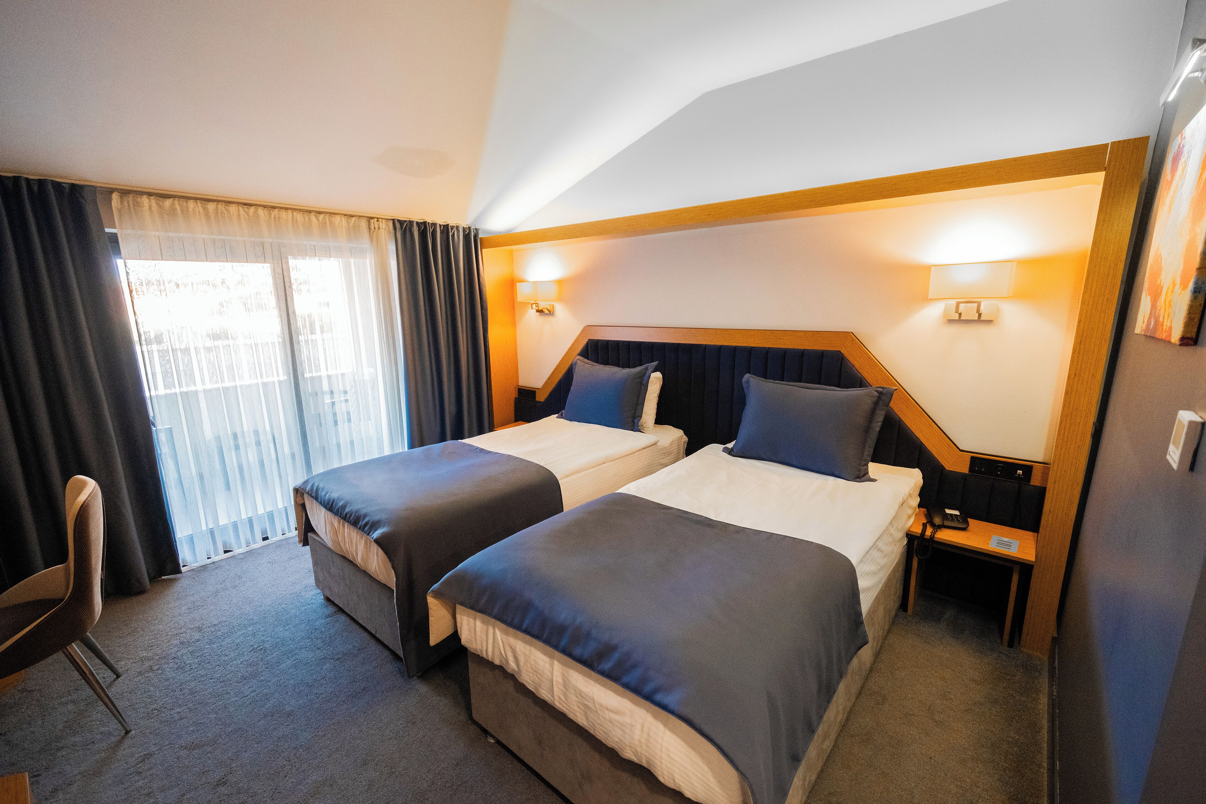 A hotel room with two beds, a desk, a chair, and a window with curtains.