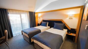 A hotel room with two beds, a desk, a chair, and a window with curtains.