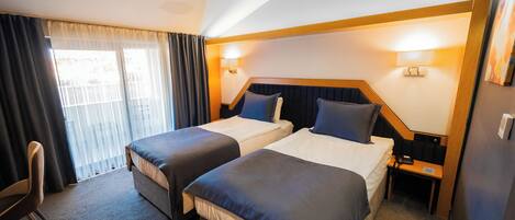 A hotel room with two beds, a desk, a chair, and a window with curtains.