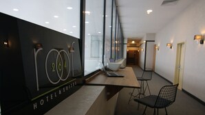 A modern hotel lobby with a reception desk, seating area, and a staircase leading to other floors.