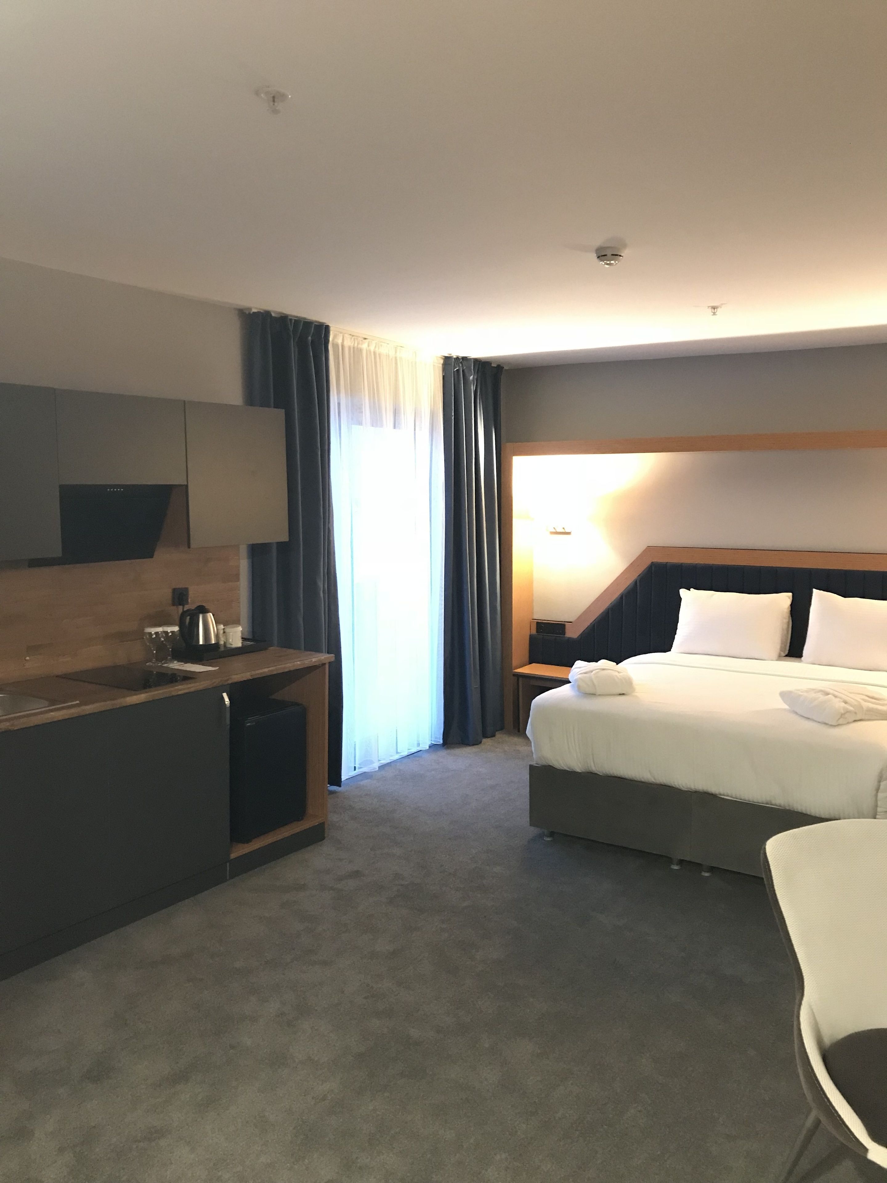 A hotel room with a bed, a desk, a chair, a nightstand, and a lamp.