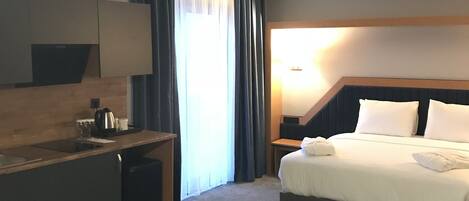 A hotel room with a bed, a desk, a chair, a nightstand, and a lamp.