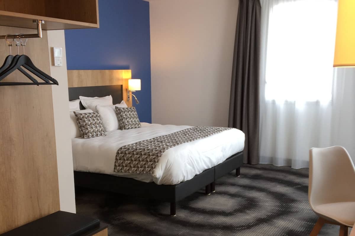A hotel room with a bed, a desk, a chair, a wardrobe, and a window with curtains.