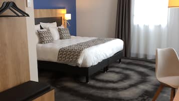 A hotel room with a bed, a desk, a chair, a wardrobe, and a window with curtains.