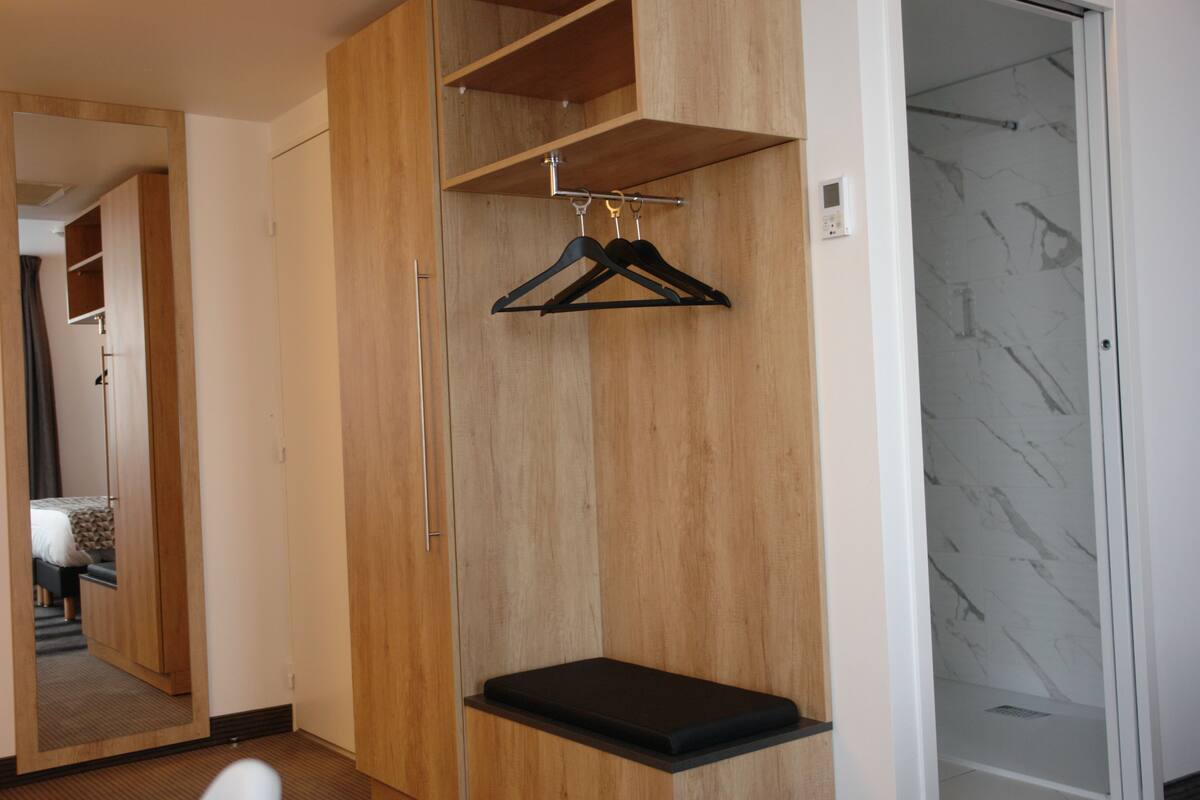 A room with a wooden wardrobe, a bench, and a hanging clothes rack.