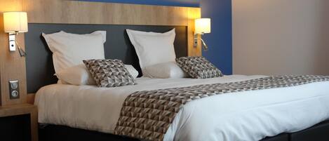 Una habitación de hotel con una cama grande, dos lámparas de noche, un cabecero de madera y una pared azul decorativa.