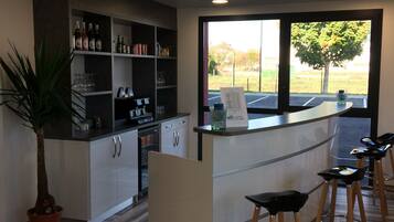 A modern bar area with a counter, stools, and shelves stocked with bottles and glasses.