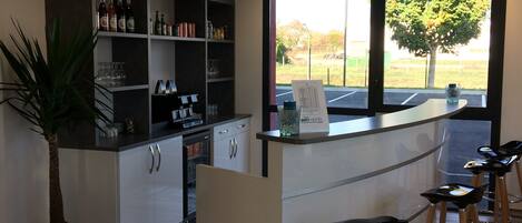Un espace bar moderne, doté d’un comptoir, de tabourets et d’étagères remplies de bouteilles et de verres.