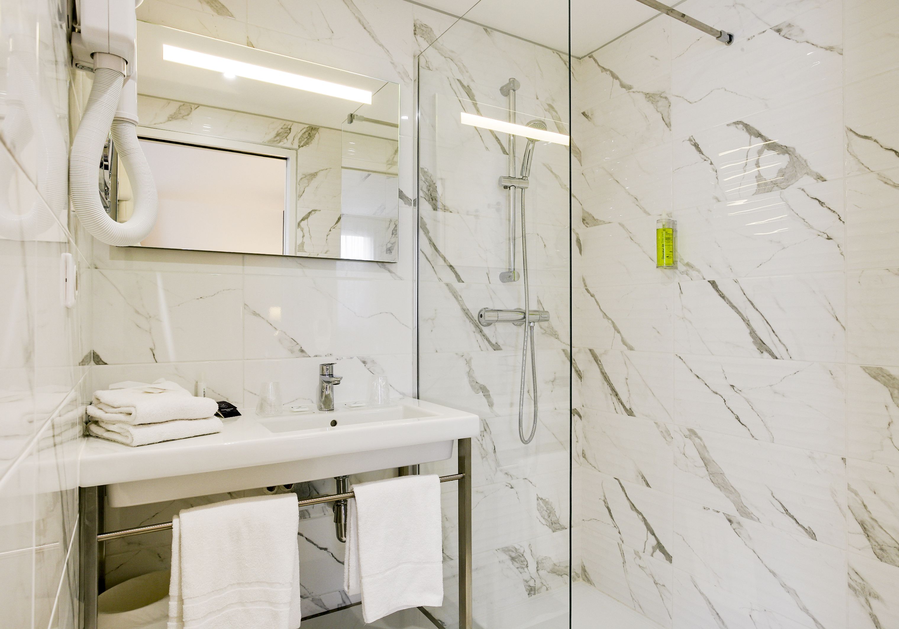 A modern bathroom with a marble wall, a sink with a mirror, and a shower area.
