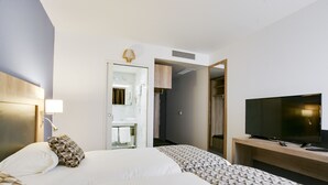 A hotel room with a large bed, a TV on a wooden stand, and a bathroom visible through an open door. - Brit Hotel Confort Loches (Loches)