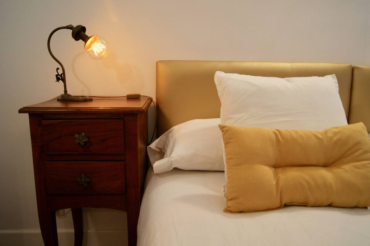 A bed with a headboard, a bedside table with a lamp, and two pillows.