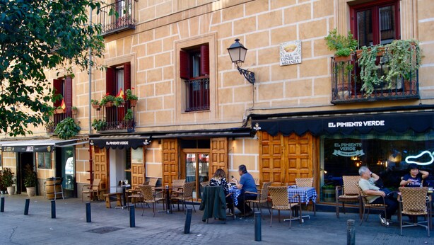 Un café con terraza, persianas de madera y plantas en macetas.