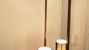 Un baño con espejo, dos lámparas cilíndricas y un mueble de tocador de madera.