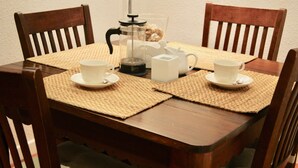 Una mesa de comedor de madera con cuatro sillas, una cafetera, una jarra de vidrio y dos tazas blancas sobre individuales.