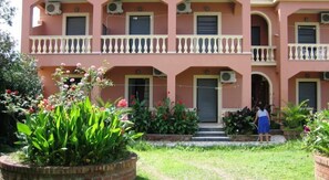 A multi-story building with balconies, air conditioning units, and a person standing at the entrance. - Makris Apartments (Corfu)