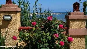 Eine Steinmauer mit einem Metallgitter, umgeben von üppigem Grün und rosa Blüten.