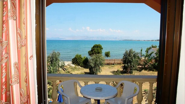 Ein Balkon mit Tisch und Stühlen, der auf ein Gewässer und eine entfernte Küstenlinie blickt.