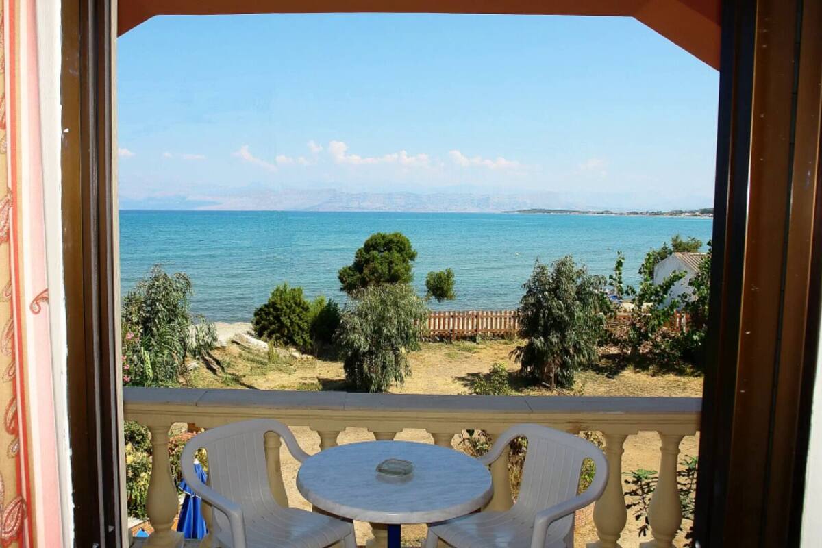 A balcony with a table and chairs, overlooking a body of water and a distant shoreline.
