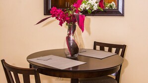 Comedor con una mesa redonda, dos sillas, un florero con flores y un espejo en la pared.