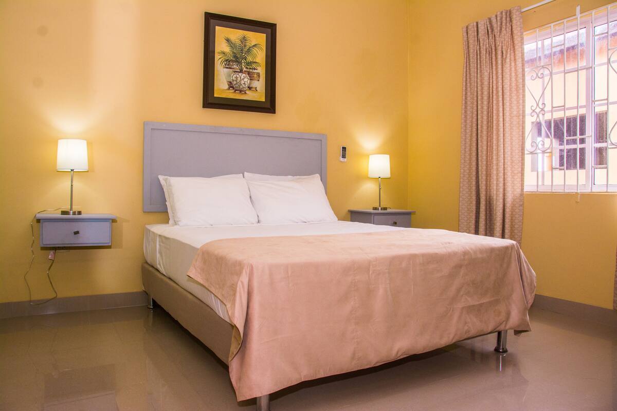 A hotel room with a bed, bedside tables, lamps, a picture on the wall, and a window with curtains.