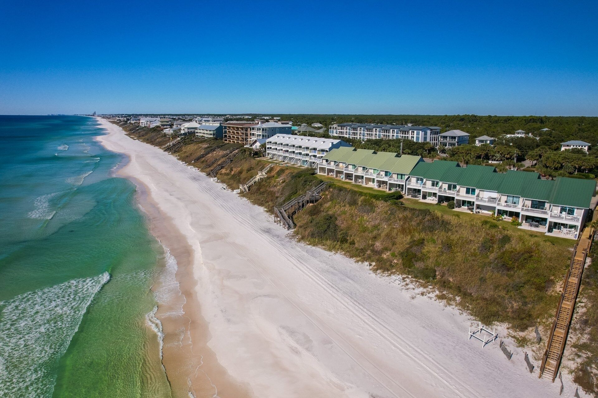 An aerial view of a coastal hotel with multiple buildings, a beach, and a clear sky.