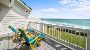A wooden deck with blue and yellow Adirondack chairs, overlooking a beach with clear turquoise water and a grassy area. - Seacrest - 6 - 2 Br townhouse by RedAwning (Panama City Beach)