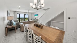 A modern kitchen with a wooden dining table, white chairs, and a chandelier. - Seacrest - 6 - 2 Br townhouse by RedAwning (Panama City Beach)