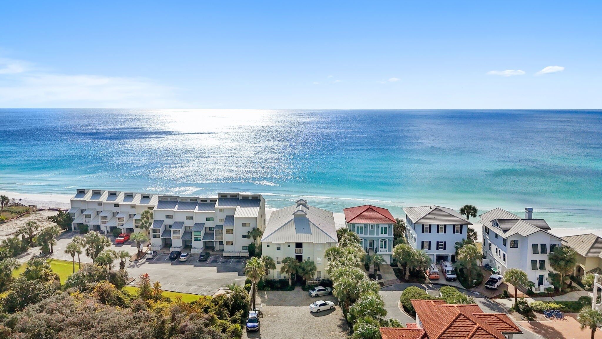 A beachfront hotel with multiple buildings, a parking area, and a view of the ocean.