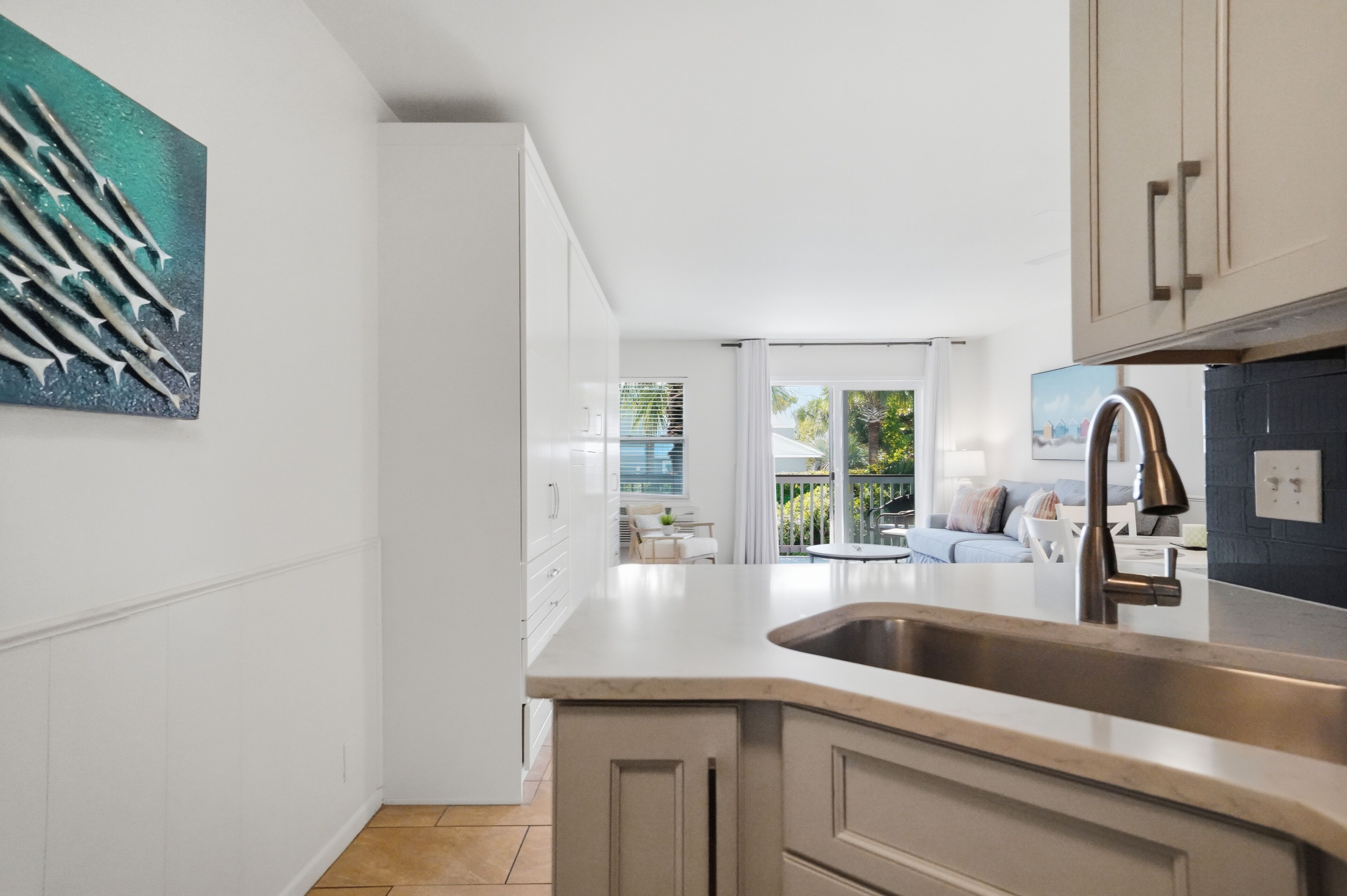 Una cocina moderna con una isla grande, armarios blancos y vistas a un balcón.