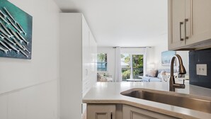 Eine moderne Küche mit einer großen Kochinsel, weißen Schränken und Blick auf einen Balkon.