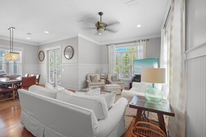 A spacious living room with a white sofa, a dining area with a table and chairs, and a television on a stand. - Pompano Palace - 4 Br home by RedAwning (Panama City Beach)