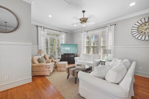 A living room with a flat-screen TV, two sofas, a coffee table, and a large wall clock. - Pompano Palace - 4 Br home by RedAwning (Panama City Beach)