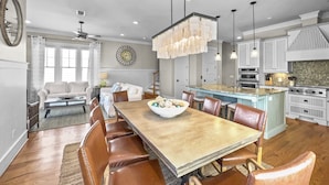 A spacious kitchen with a central island, wooden dining table, and modern pendant lighting.