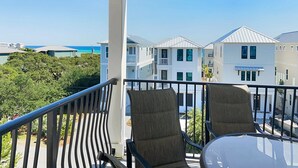 A balcony with two chairs and a table, overlooking a coastal area with buildings and greenery.