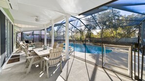 Une terrasse couverte avec une piscine, du mobilier d’extérieur et une vue sur le jardin arrière.