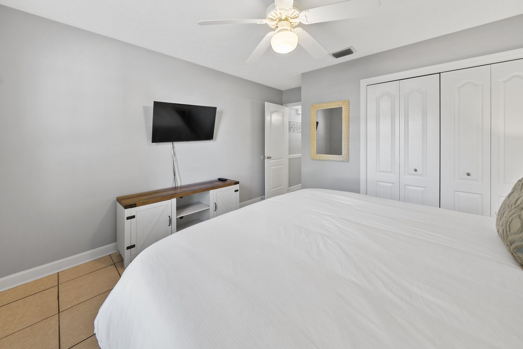 A bedroom with a bed, a TV mounted on the wall, a ceiling fan, and a wardrobe.