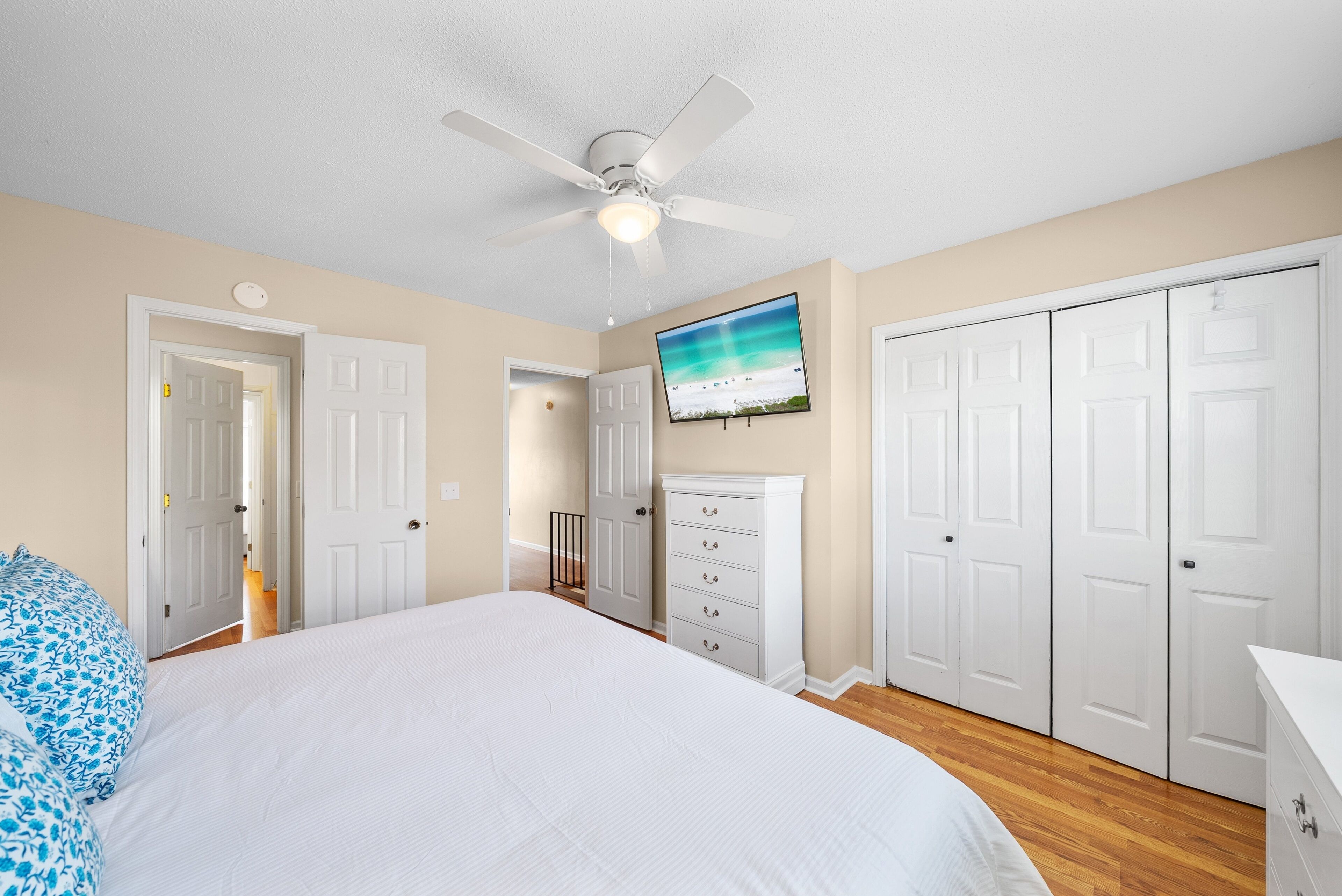 A bedroom with a bed, a ceiling fan, a dresser, and a TV on the wall.